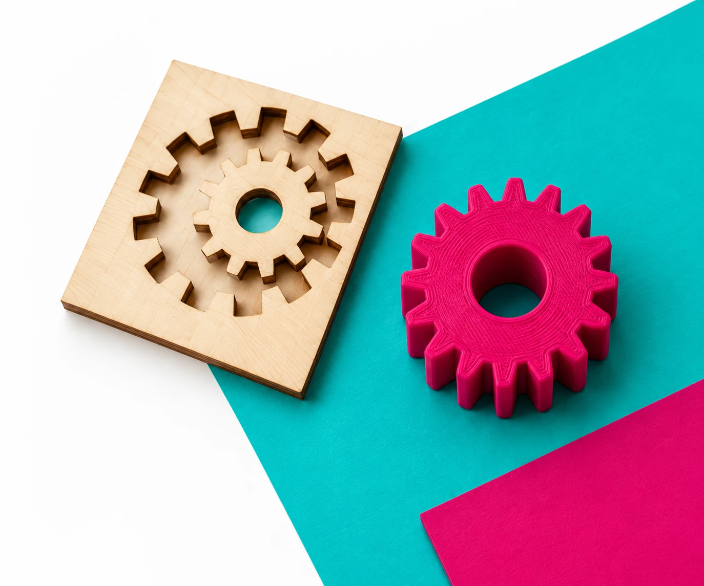 Engrenage en bois découpé au laser et engrenage magenta imprimé en 3D sur fond turquoise